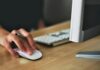 Free A hand using a wireless mouse at a modern desk setup with a computer and keyboard. Stock Photo