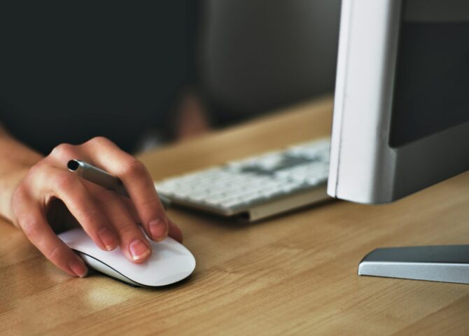 Free A hand using a wireless mouse at a modern desk setup with a computer and keyboard. Stock Photo