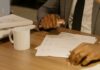 Free Close-up of a businessman holding and reviewing documents on a wooden desk. Stock Photo