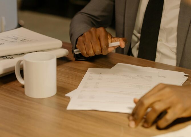 Free Close-up of a businessman holding and reviewing documents on a wooden desk. Stock Photo
