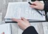 Free Close-up of hands analyzing insurance policy paperwork with pen on table. Stock Photo
