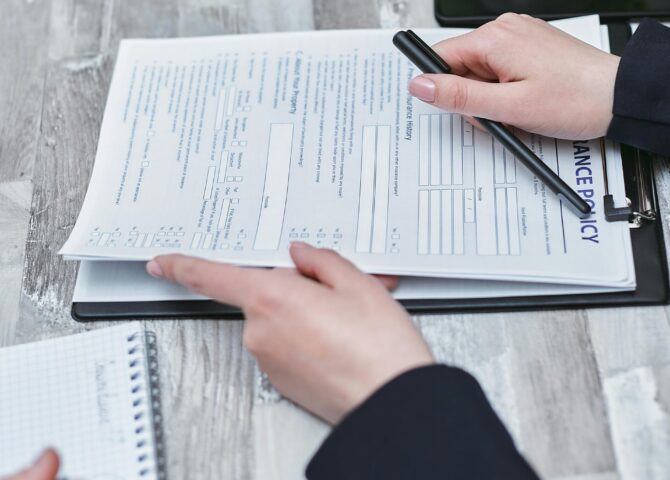 Free Close-up of hands analyzing insurance policy paperwork with pen on table. Stock Photo